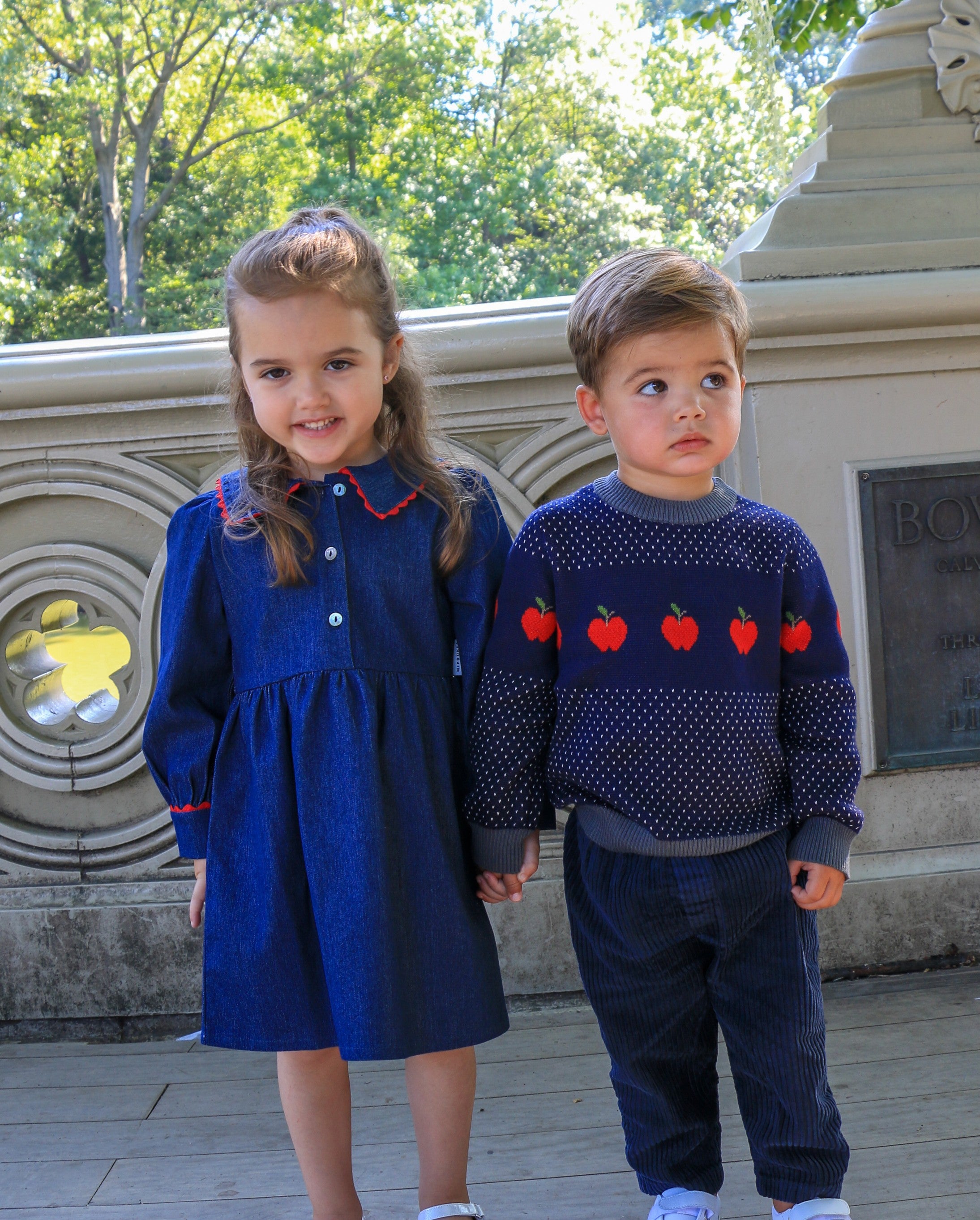 young girl wearing a denim dress and young bo wearing an apple sweater holding hands