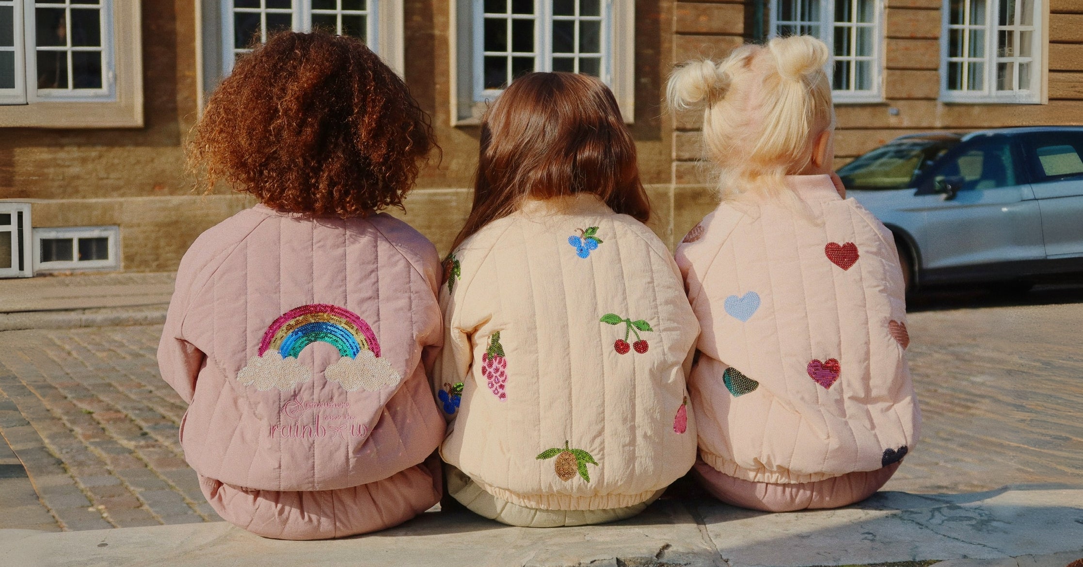 3 girls wearing konges slojd outerwear sitting on sidewalk