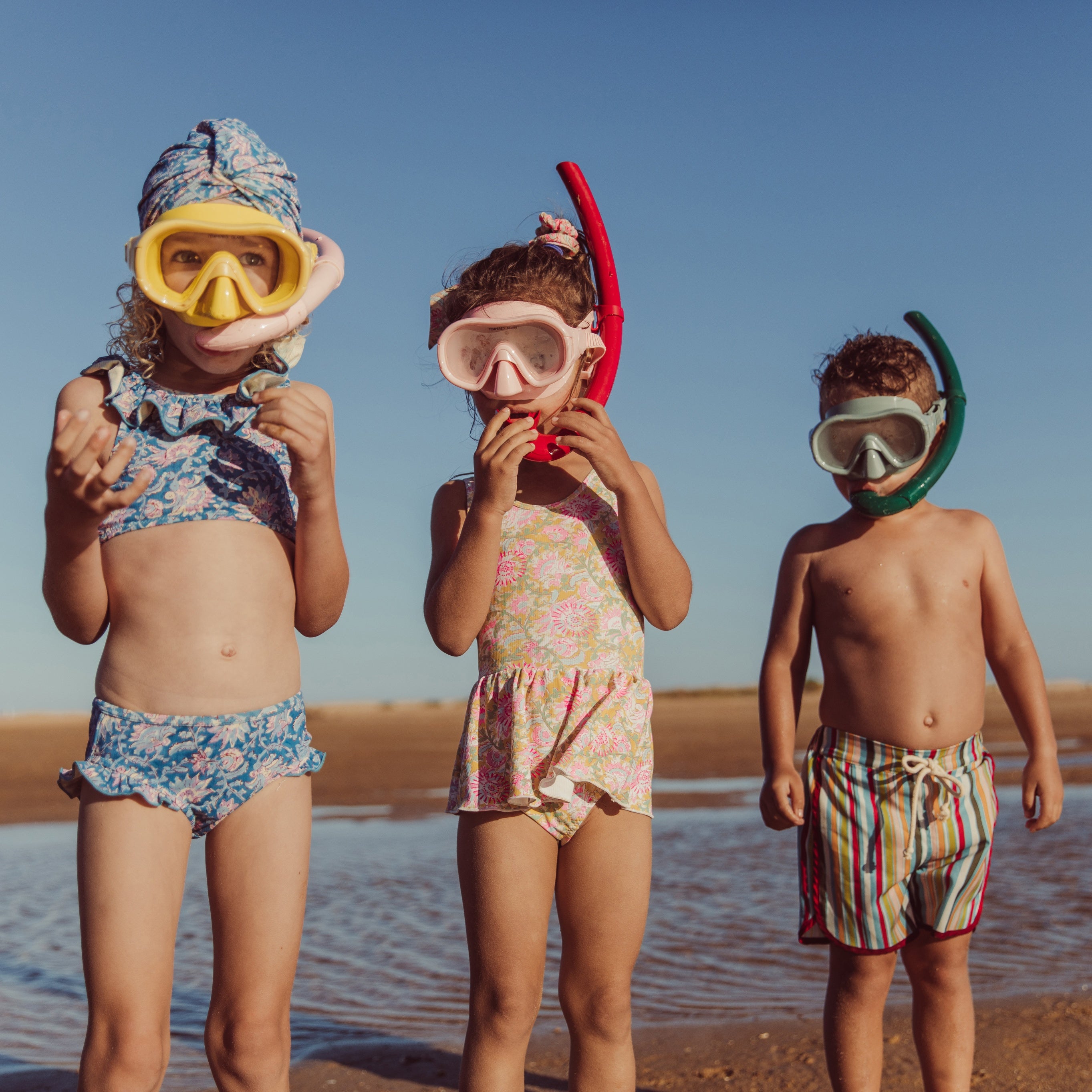 3 kids wearing swim on the beach with goggles on