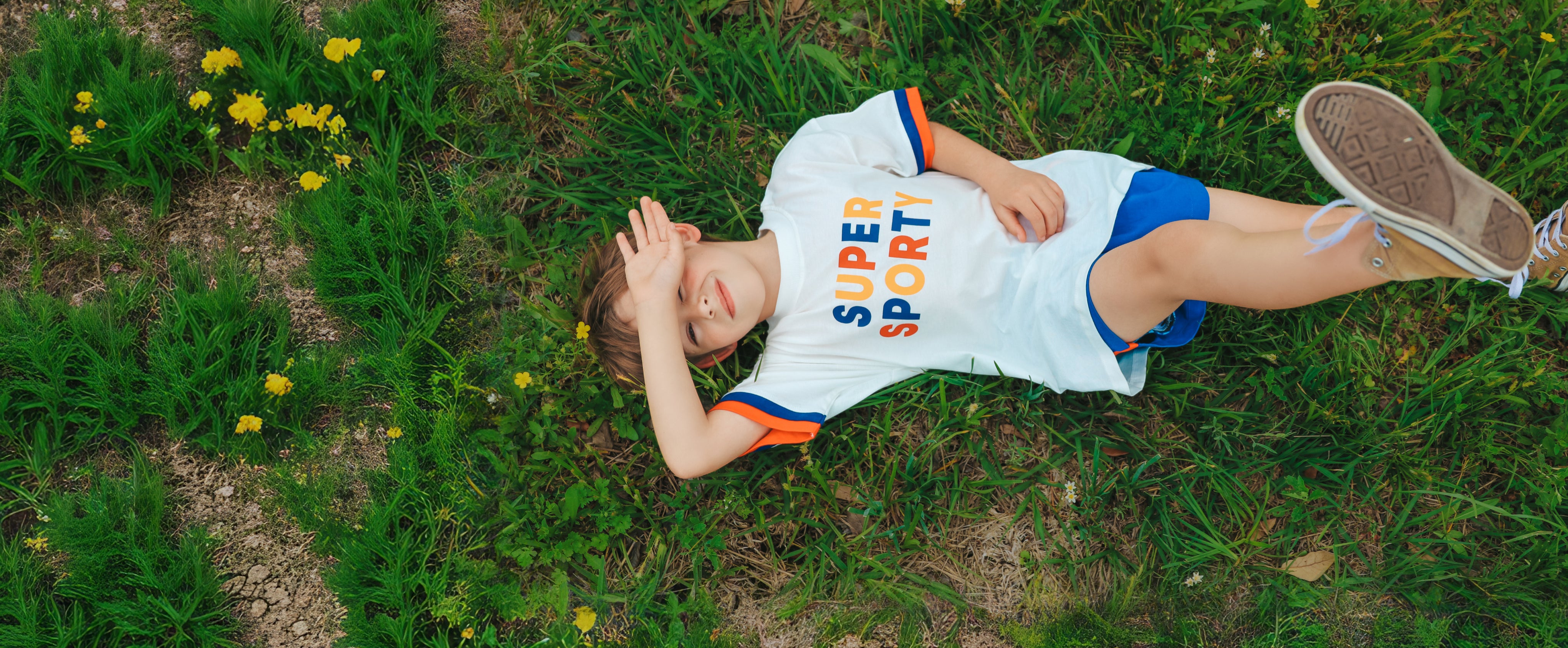 boy laying in grass wearing super sporty tee