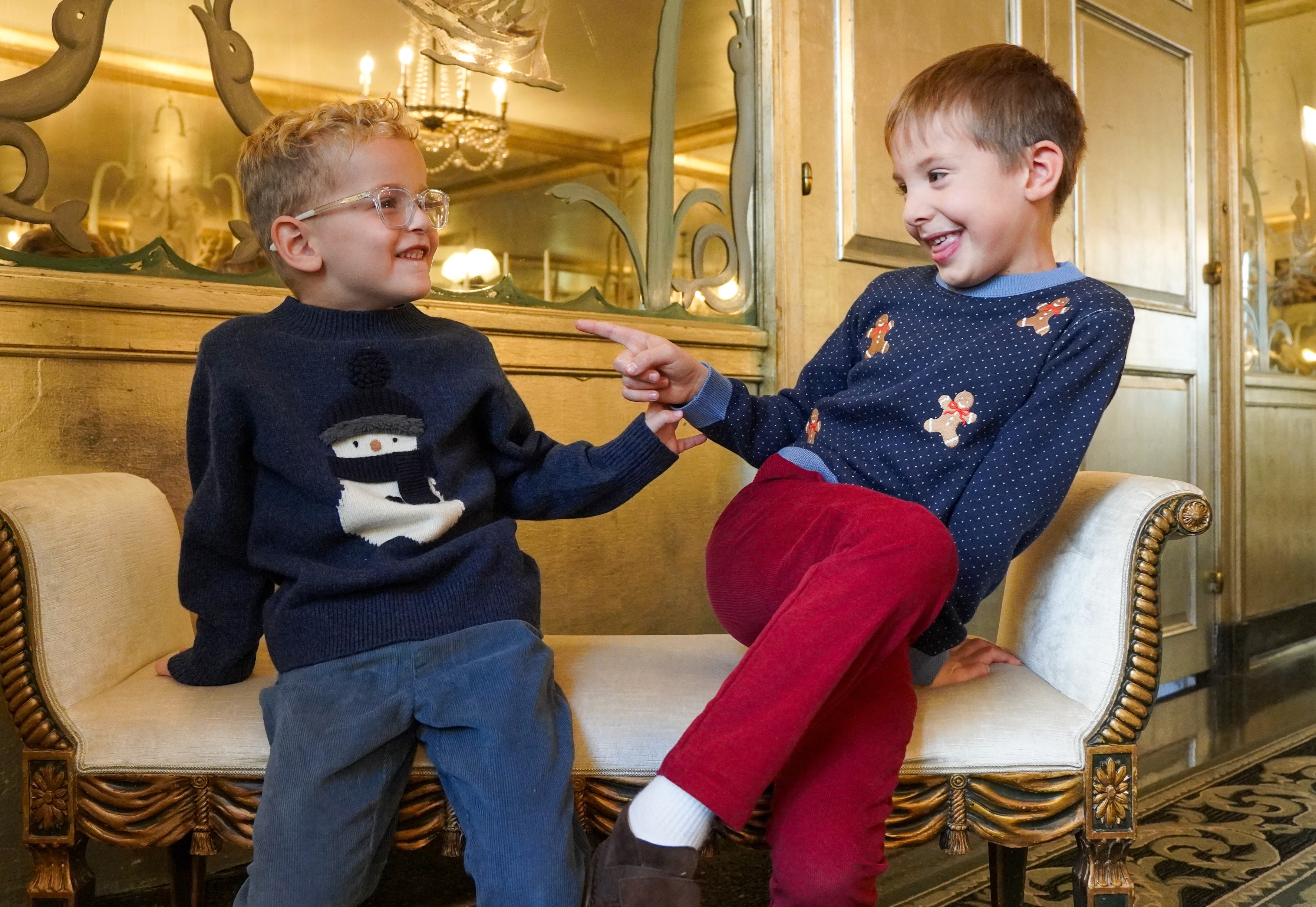 two boys pointing and laughing at eachother wearing holiday sweaters