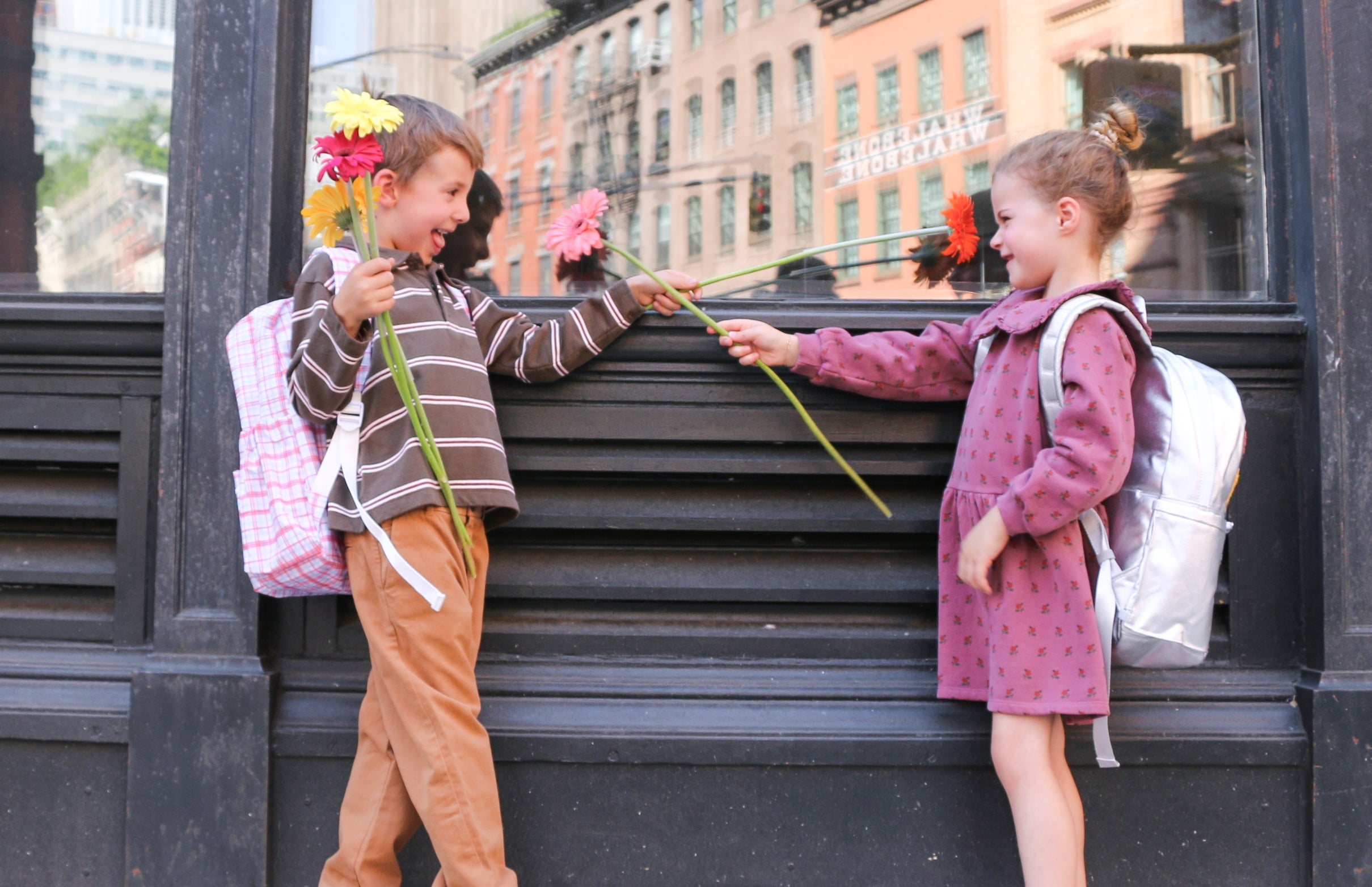young girl and boy wearing danrie clothes and backpacks holding flowers