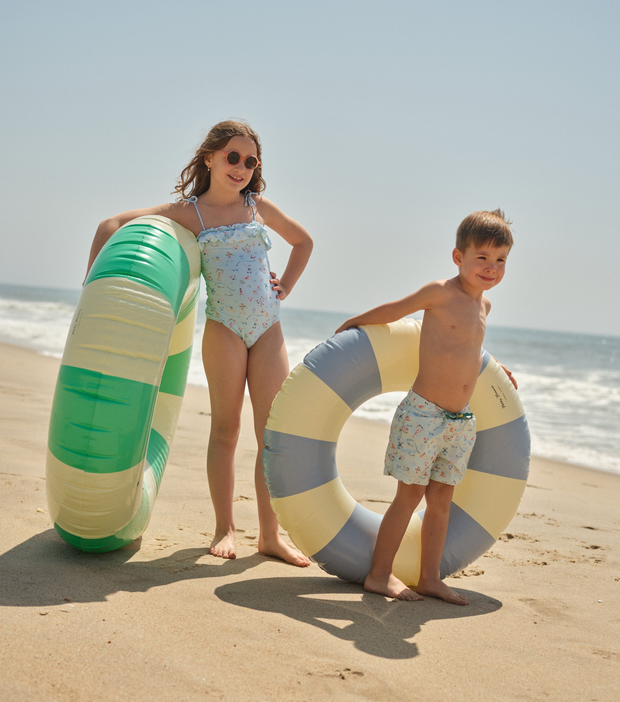 two kids holding swim tubes on the beach