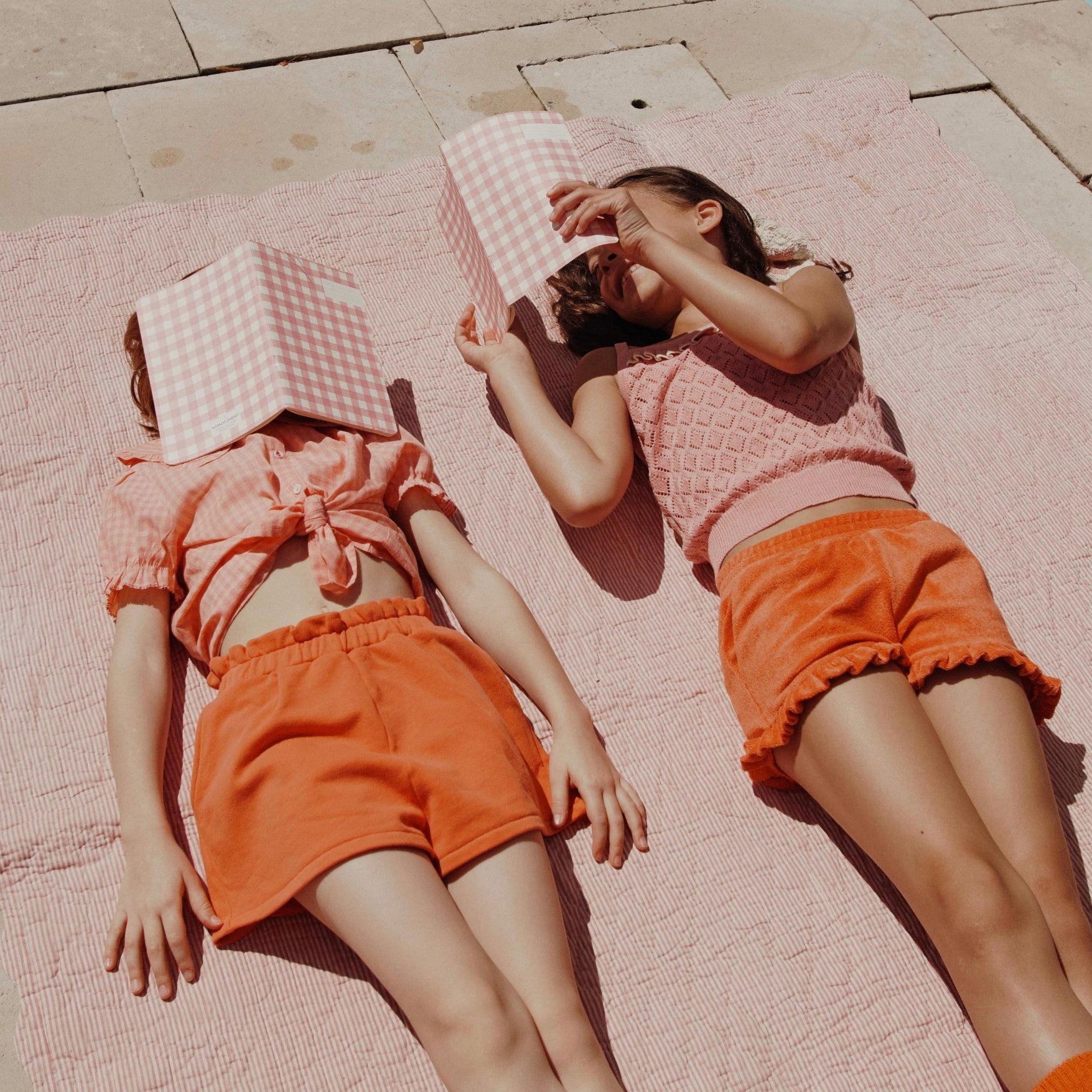 two girls laying on a towel reading a book