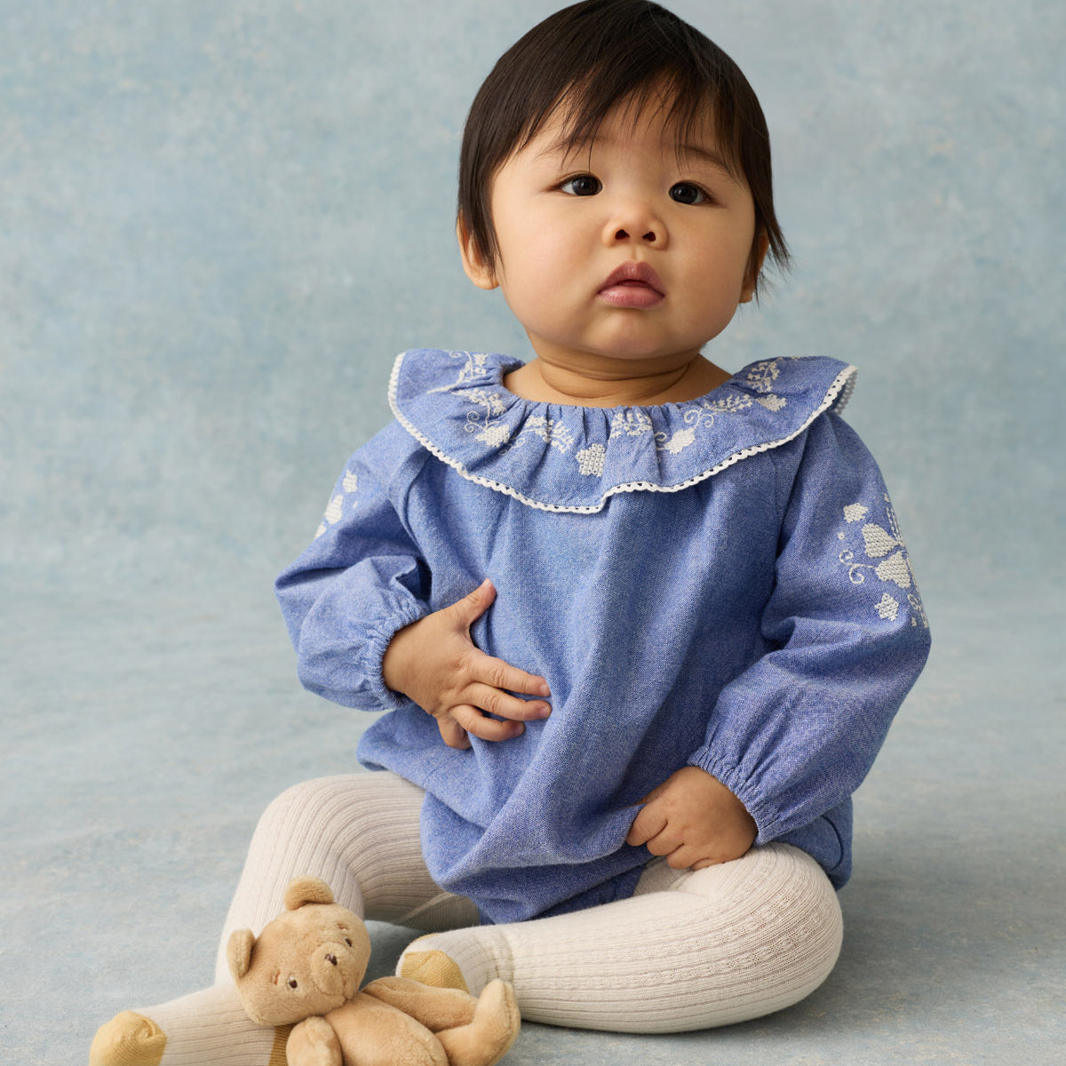 newborn baby wearing a lilac romper sitting down