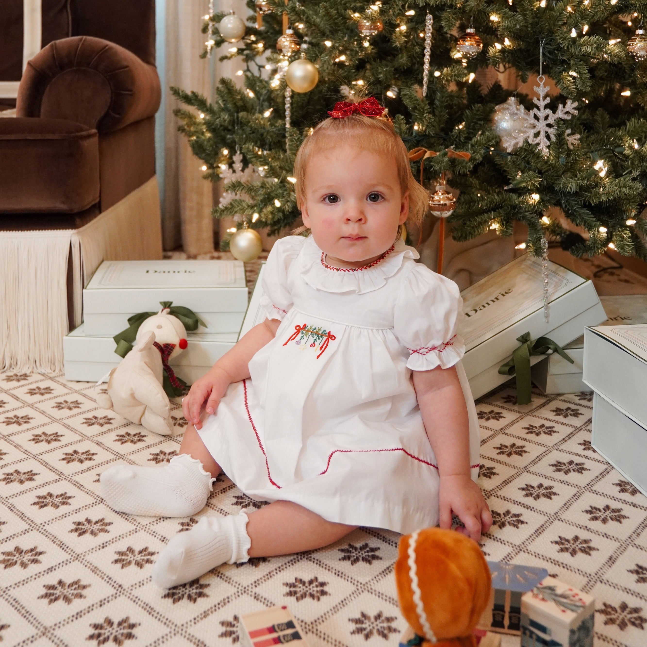 baby girl in front of christmas tree in white holiday dress