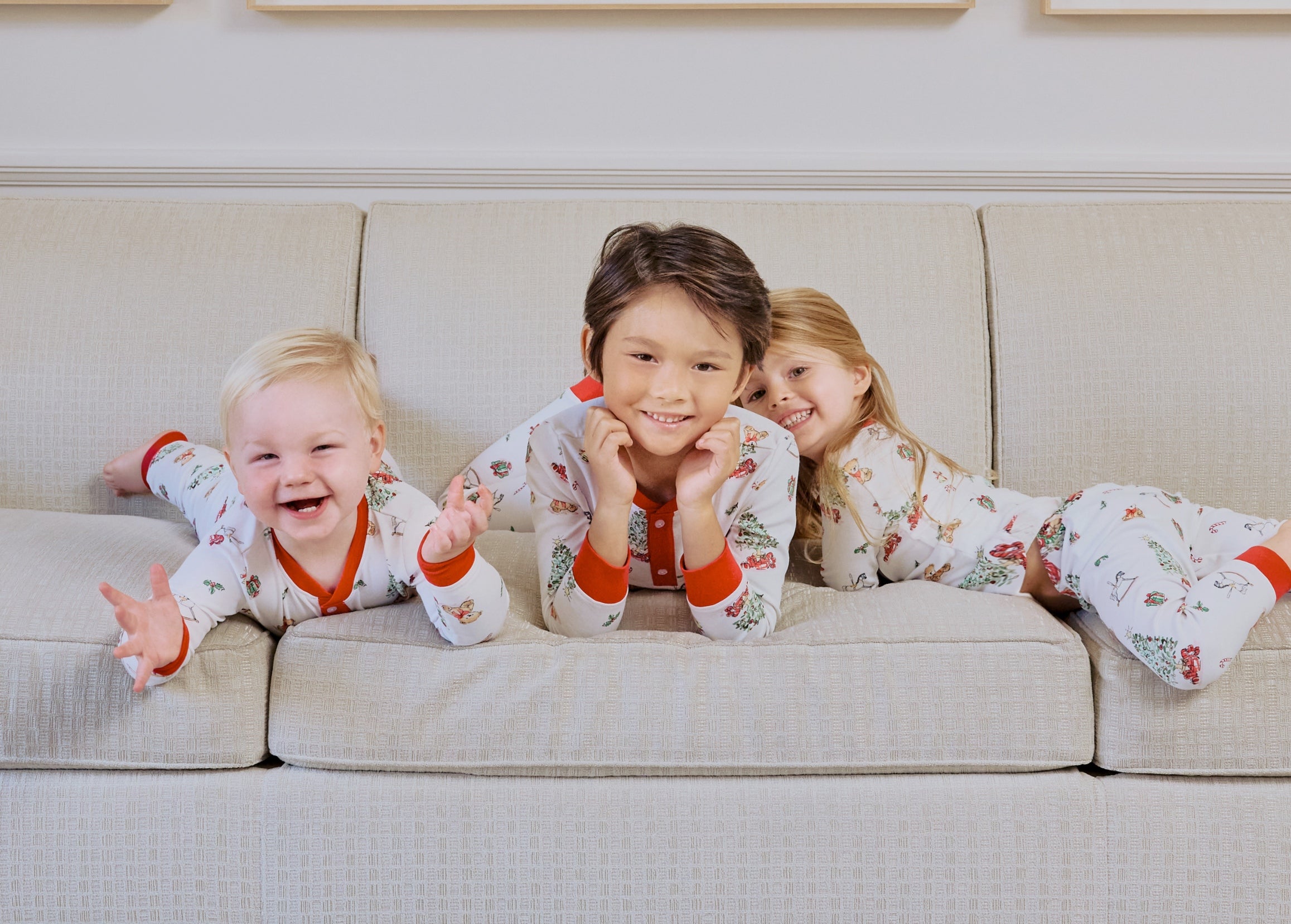 3 young kids on a couch wearing matching holiday pajamas