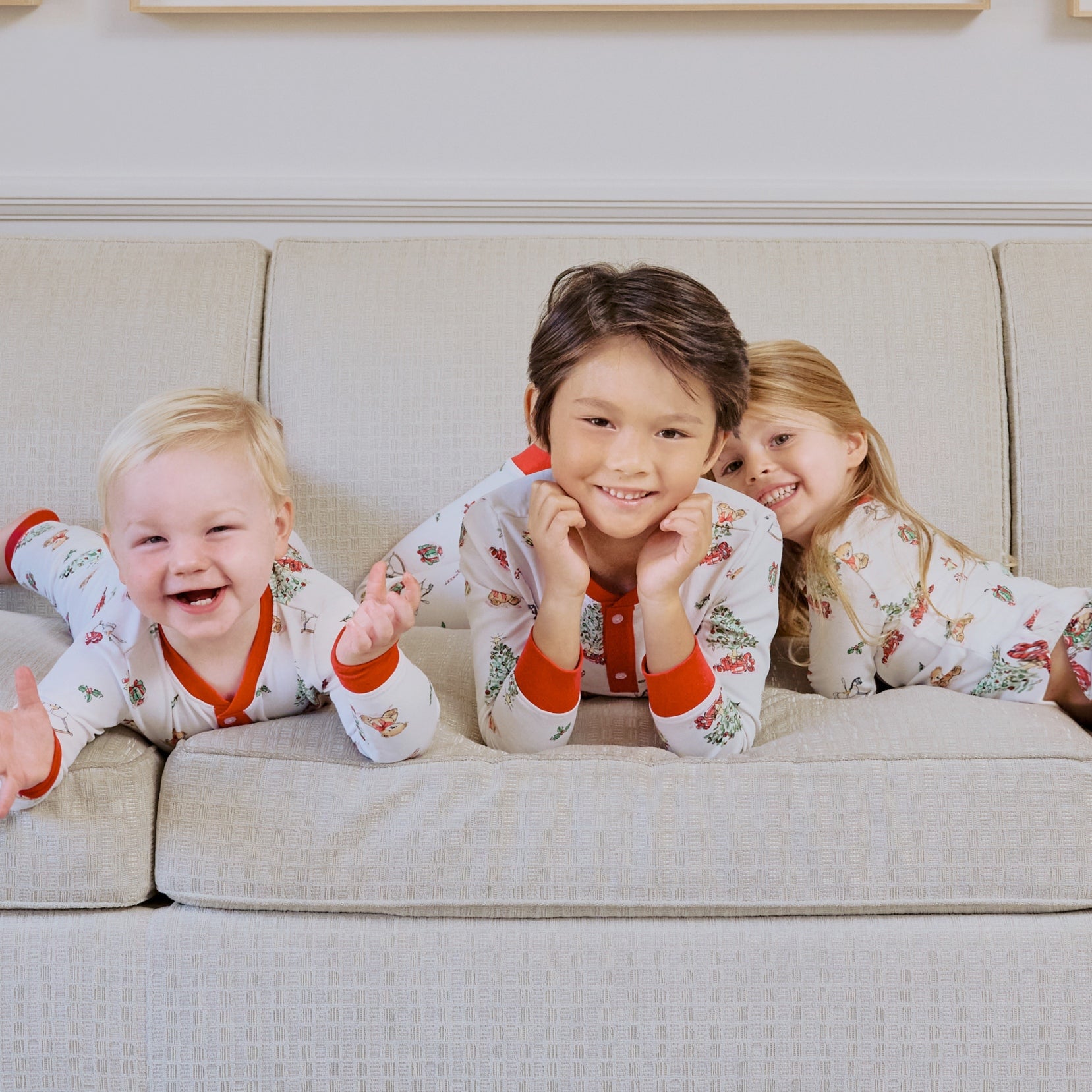 3 young kids on a couch wearing matching holiday pajamas